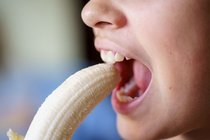 Crop of girl with mouth open eating fresh peeled banana