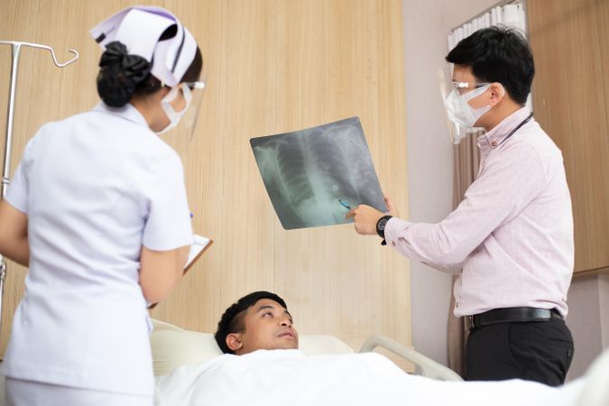 Patient lying in hospital bed with medical professionals showing chest X-ray