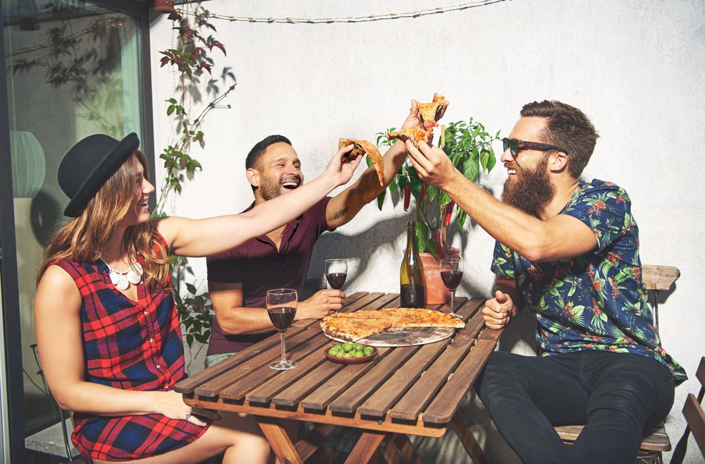 Three friends smiling and holding up pizza slices