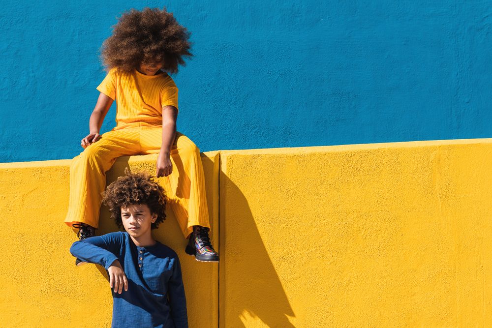 Black curly haired girl and boy resting near colorful wall