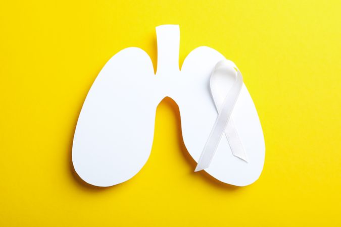 Lung shape cut out of paper with ribbon on yellow background