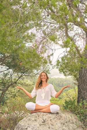Happy woman practicing meditation on stone in forest