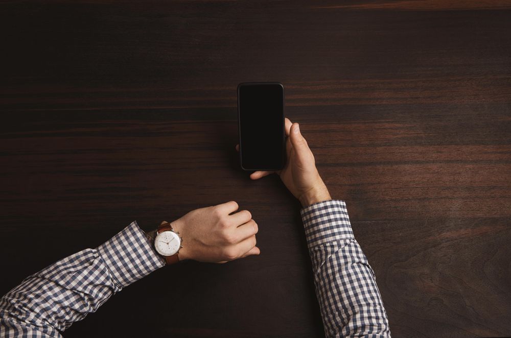 Arms in plaid shirt checking watch and holding cell phone
