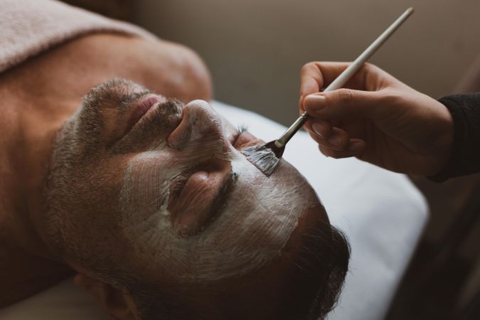 Person applying cream on man's face at spa