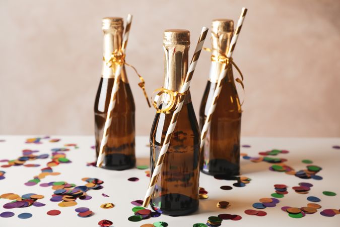 Mini champagne bottles with straws on decorated background, close up