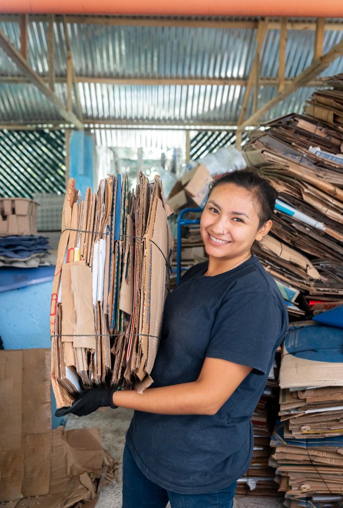 Young Hispanic Woman Smiling While Holding A Heavy Cardboard Pile