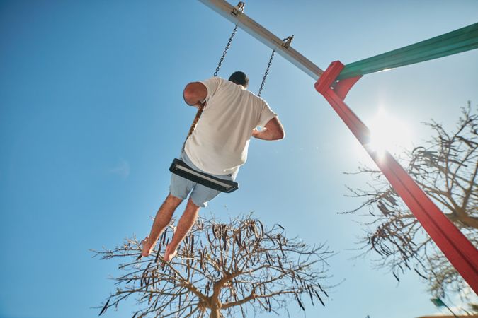 Man swinging on playground in sunlight