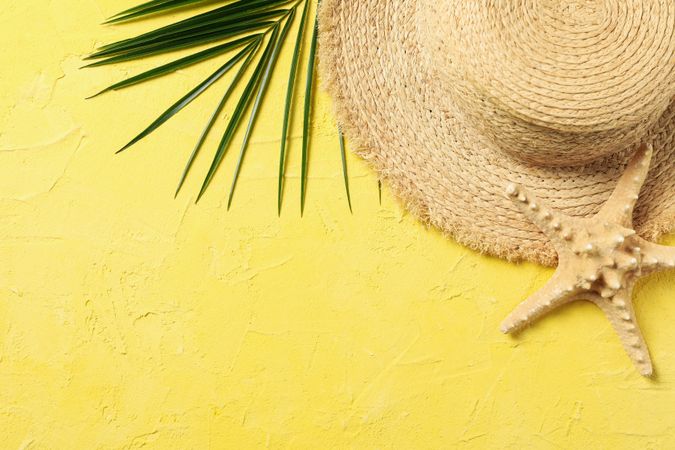 Straw hat, palm branch and starfish on yellow background, top view