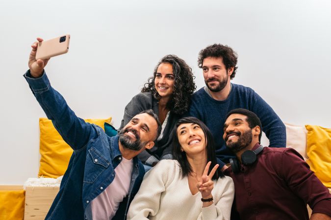 Multiracial happy coworkers taking a selfie with smartphone in the break room of a modern coworking office