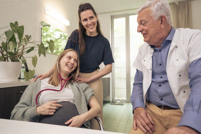 Happy lesbian couple listening to baby's heartbeat with a stethoscope.