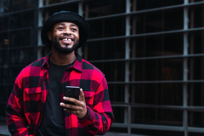 Cheerful Black male with smartphone in contemporary building