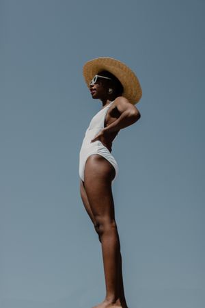 Woman standing wearing a light swimsuit and a sun hat