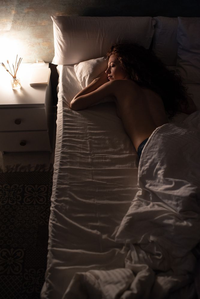 Back view of a naked woman lying down in bed