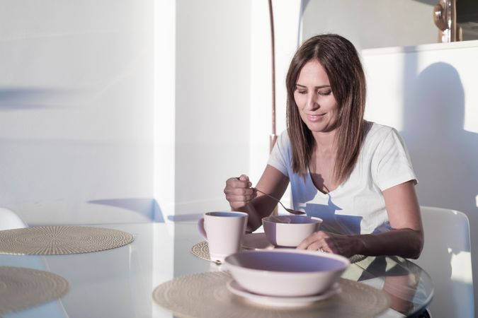 Calm woman sitting at sunny table having bowl of cereal