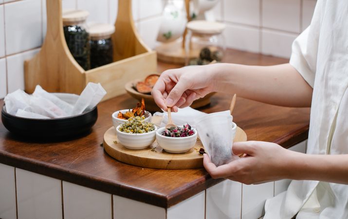 Cropped image of a person putting herbs in saucers in wooden tray in kitchen