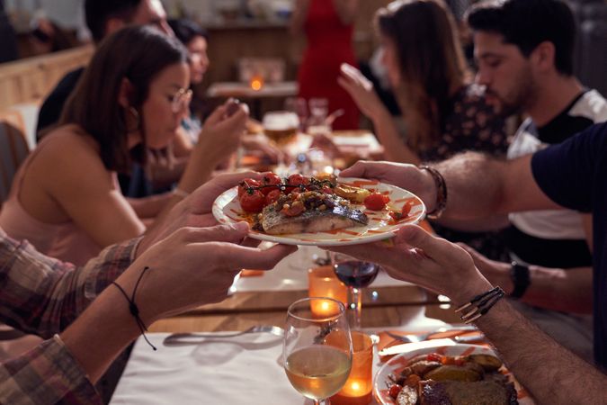 Unrecognizable people passing plate with dish near friends