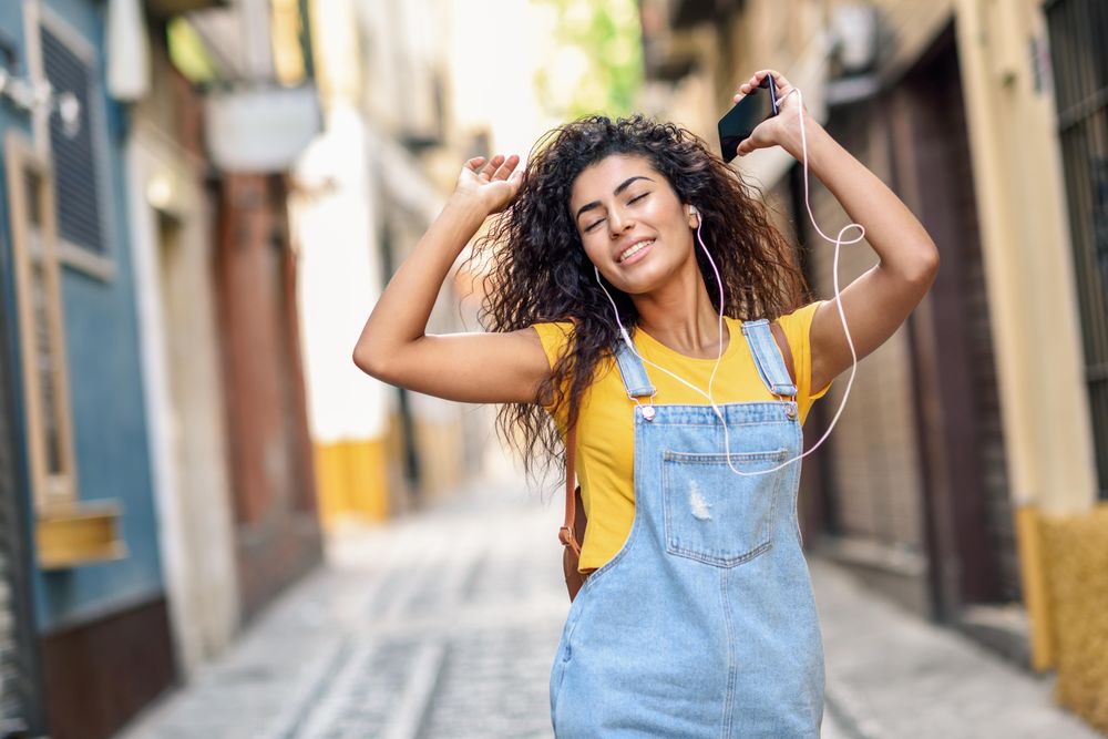 Arab woman listening to music with earphones and dancing in lane