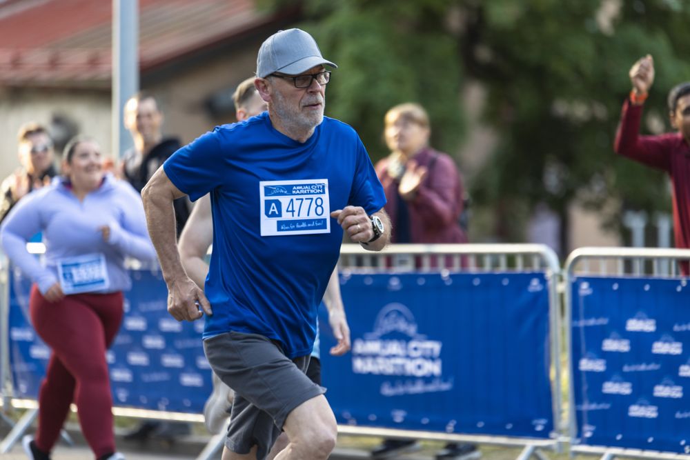 Portrait of a Mature Male Jogger Running in a City Marathon and Being Cheered for by the Audience.