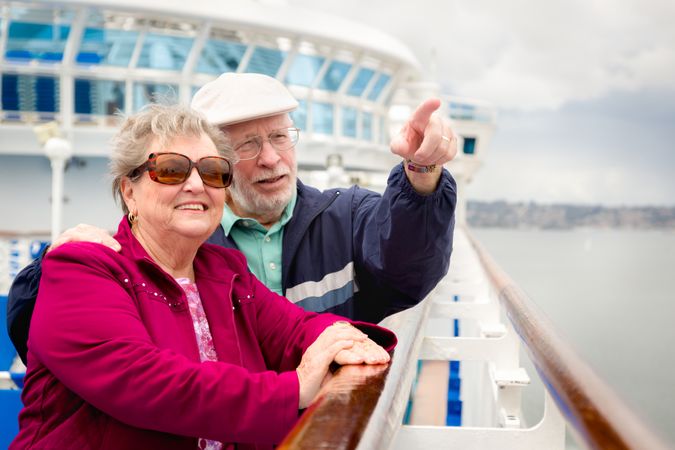 Smiling Older Adult Couple Enjoying The View From Their Passenger Cruise Ship Railing.
