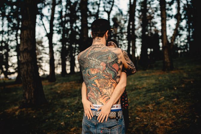 Young guy in tattoos hugging woman in forest
