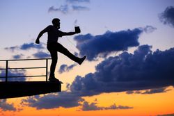 Out line of male walking off ledge with tablet against a colorful dusk side, vertical