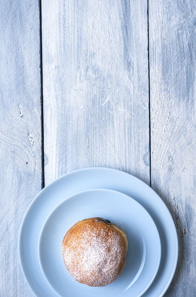 Overhead of jelly doughnut with powdered sugar on blue table