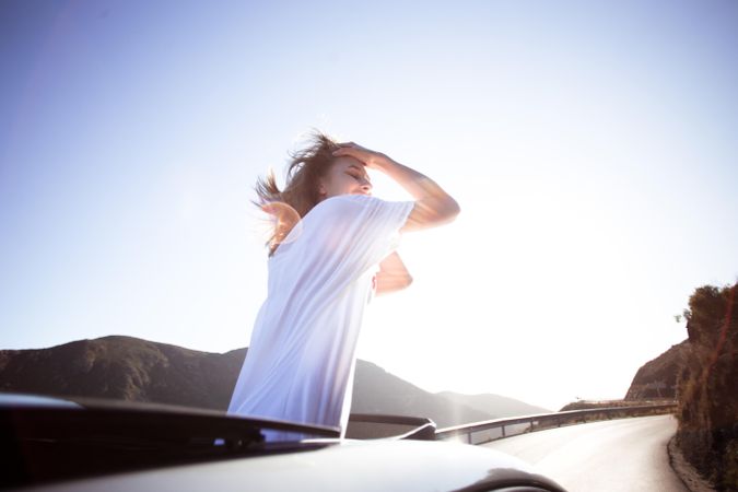 Woman standing out through a vehicle’s sunroof running her hands through her hair