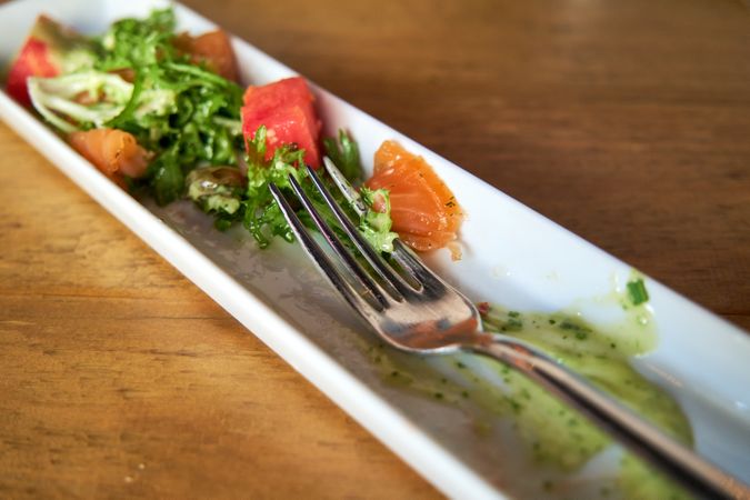 Fork in a dish of marinated salmon with escarole salad