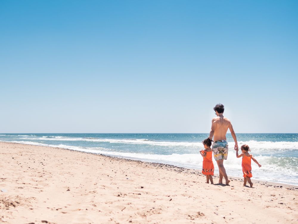 Father walking on sandy beach with toddler daughters