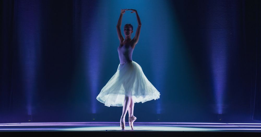 Cinematic Shot of Ballerina in Pointe Shoes and Tutu Dancing and Rehearsing on Classic Theatre Stage with Dramatic Lighting.