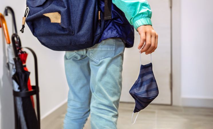 Unrecognizable boy with backpack holding mask in hand