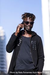 Front view of Black man with sunglasses standing against cityscape on the street while using a mobile phone in sunny day 5XrO7K