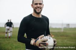 Portrait of a cheerful goalkeeper standing with a soccer ball in hand 5rLkdb
