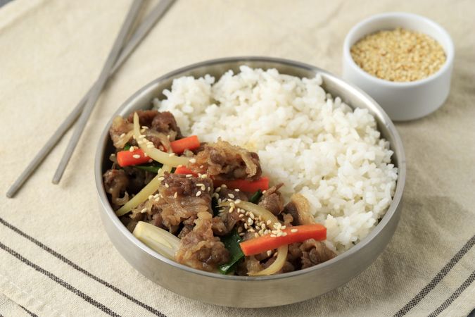 Half beef half rice bowl on table with chopsticks and sesame seeds