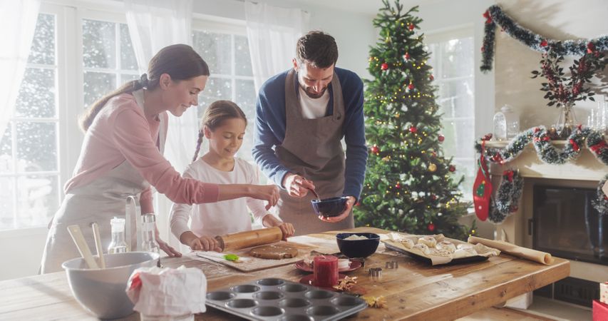 Happy Family During Christmas: Portrait of Young Parents and Their Cute Little Daughter Preparing Pastries Together at Home.