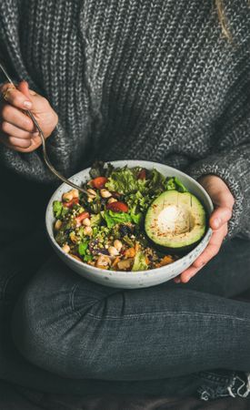 Woman in jeans and sweater holding bowl of fresh salad