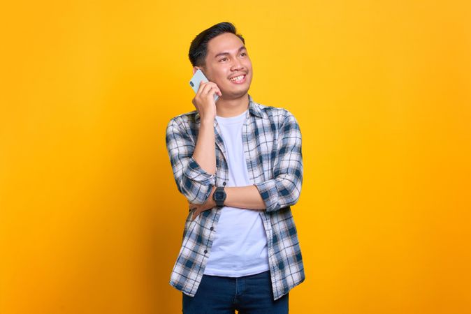 Happy Asian male talking on phone in studio shoot with arm over his chest