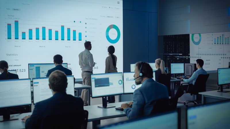 Data Analysts Examine Financial Charts on Large Screen in Modern Office.