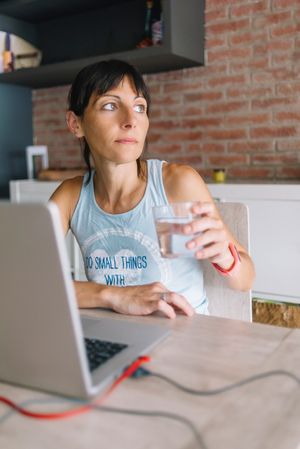Woman holding glass of water while sitting at laptop