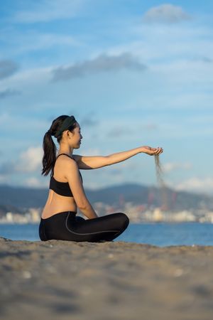 Sportive woman pouring sand through fingers on beach