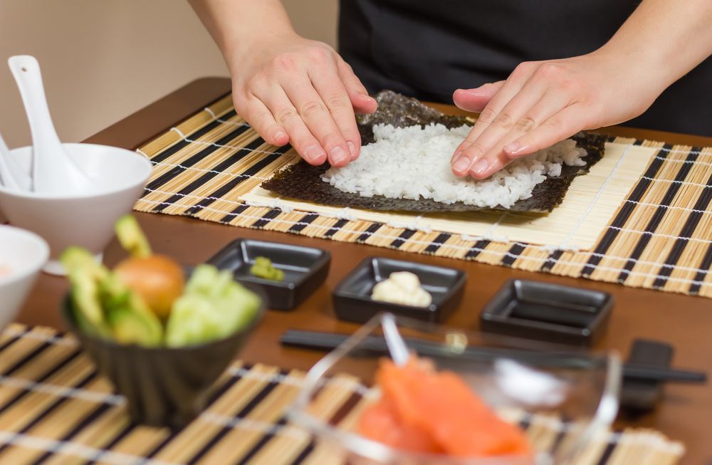 Hands of woman chef filling Japanese sushi rolls with rice on a nori seaweed sheet
