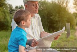 Grey haired man and child reading a newspaper outdoors 48Vvv0