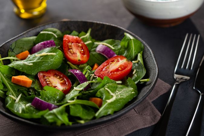 Bowl of sliced tomatoes and red onions on bed of lettuce, vertical