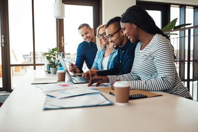 Multi-ethnic colleagues smiling around a laptop at work