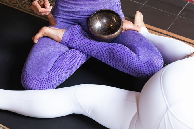 Anonymous woman playing singing bowl during yoga session with female friend
