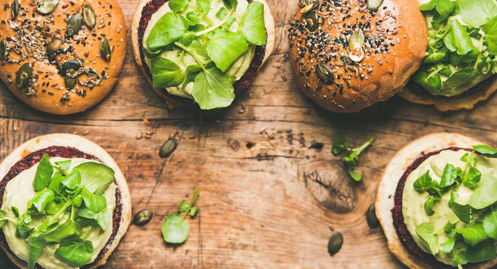 Fresh vegan burgers on seeded buns arranged on wooden board, with copy space