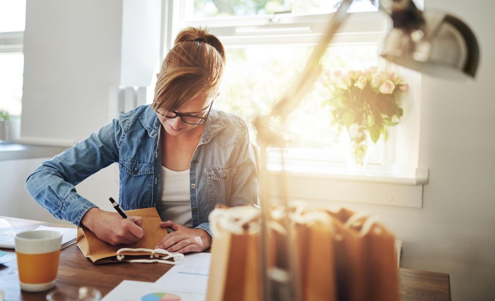 Female entrepreneur writing on bags of products while fulfilling orders from her home office