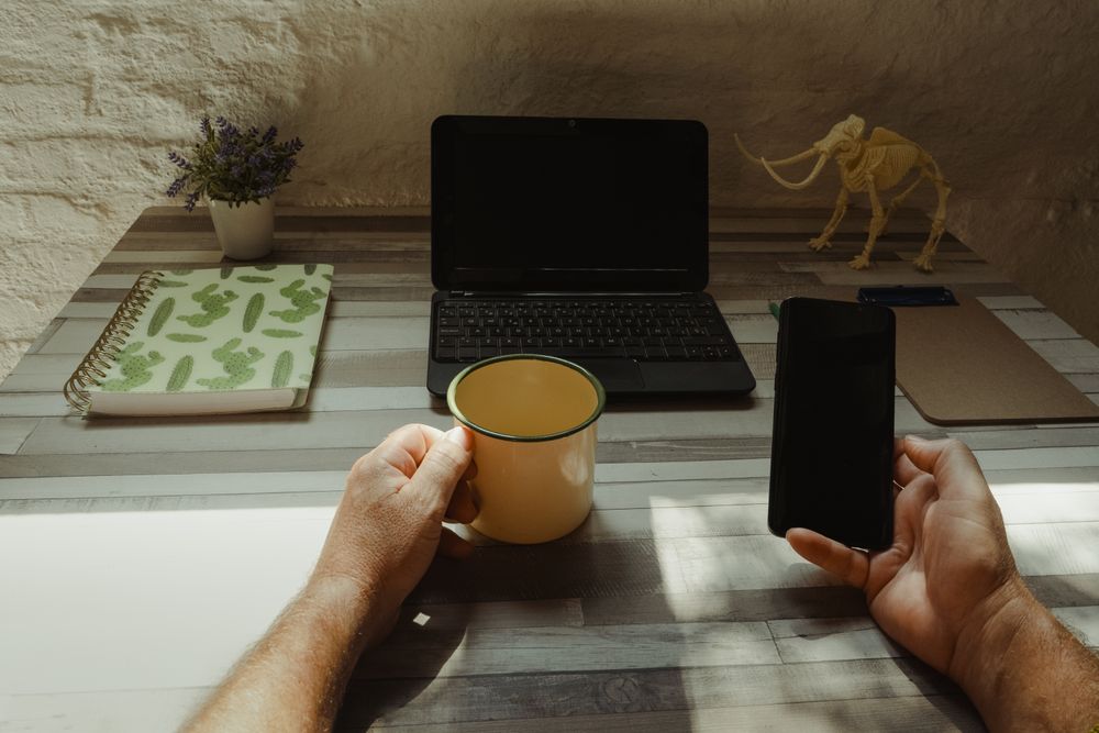 Crop freelancer with mug using smartphone