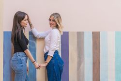 Happy girlfriends sitting against painted urban wall