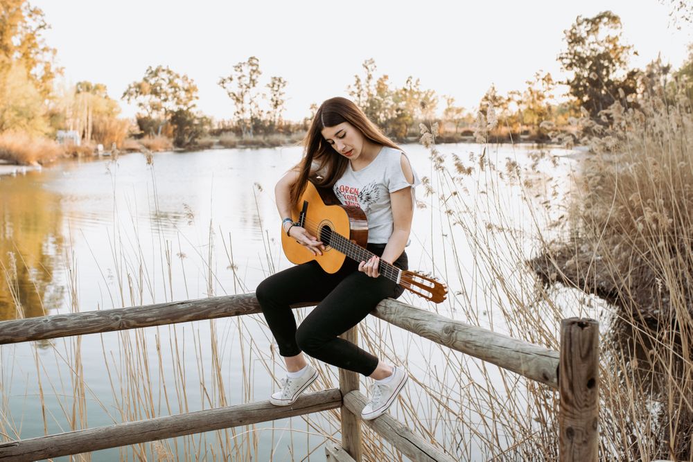 Young woman playing guitar near water